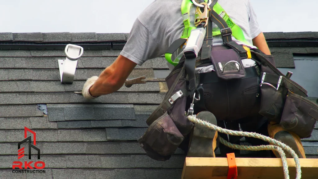 Roofer performing maintenance on an asphalt shingle roof, wearing a harness. 